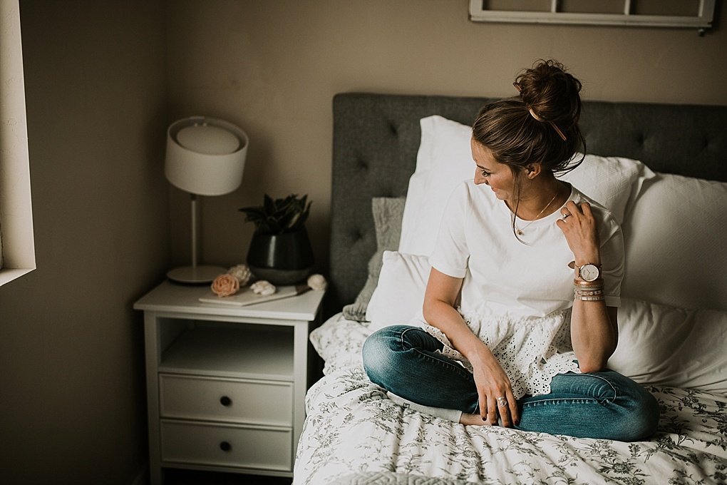 girl sitting on bed in white lace top jeans and top knot with sola wood flowers