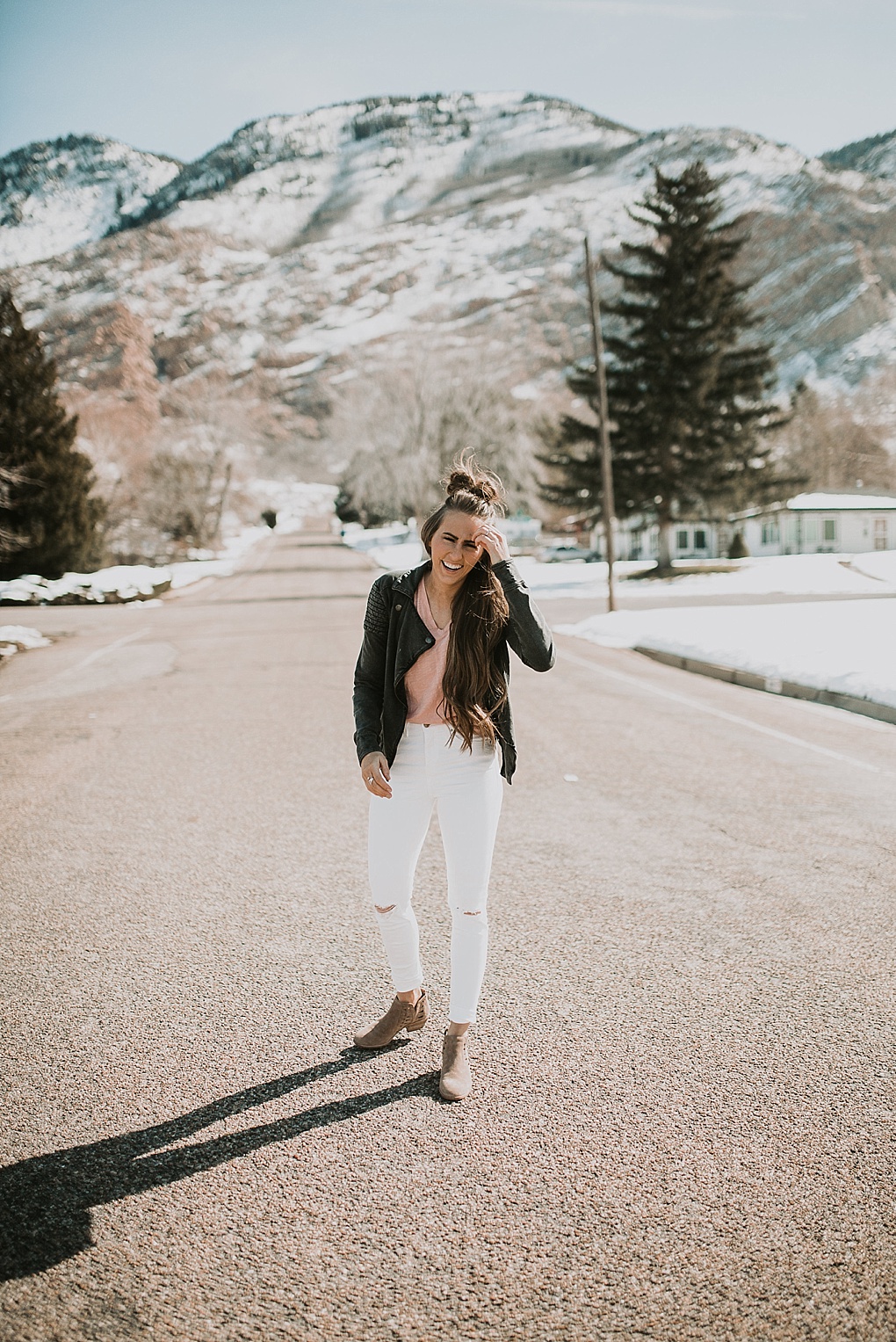 girl standing in road with white jeans on with madewell basic tee and leather jacket with hair loosely curled with half up top knot