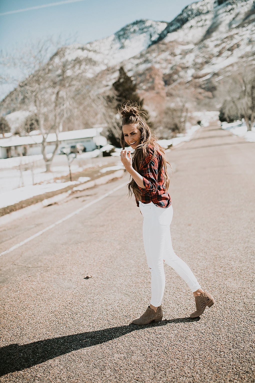 girl standing in road wearing flannel shirt with white jeans and hair loosely curled with half up top knot