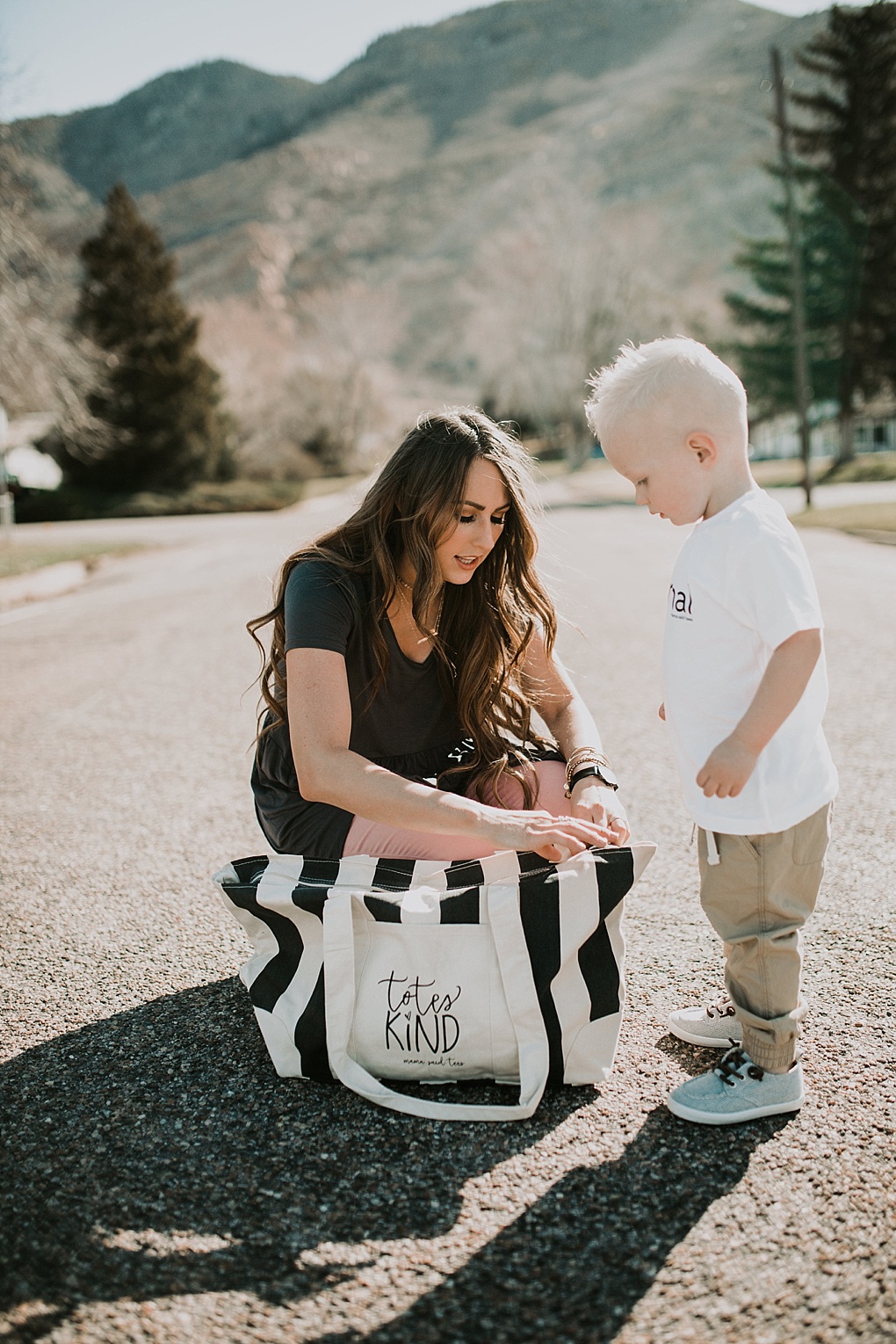 girl standing in road wearing blush jegging jeans with cents of style grey peplum with mama said tees tote bay with long loosely curled brown hair with caramel highlights little boy in white normal tee with khaki joggers and freshly picked hard sole shoes