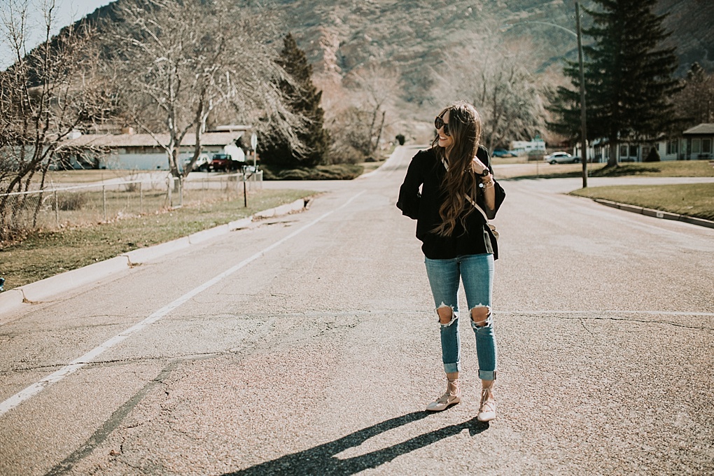 girl standing in road with karen walker sunglasses on with levi distressed high waisted jeans michael kors crossbody bag and flats on with loosely curled brown hair with caramel highlights