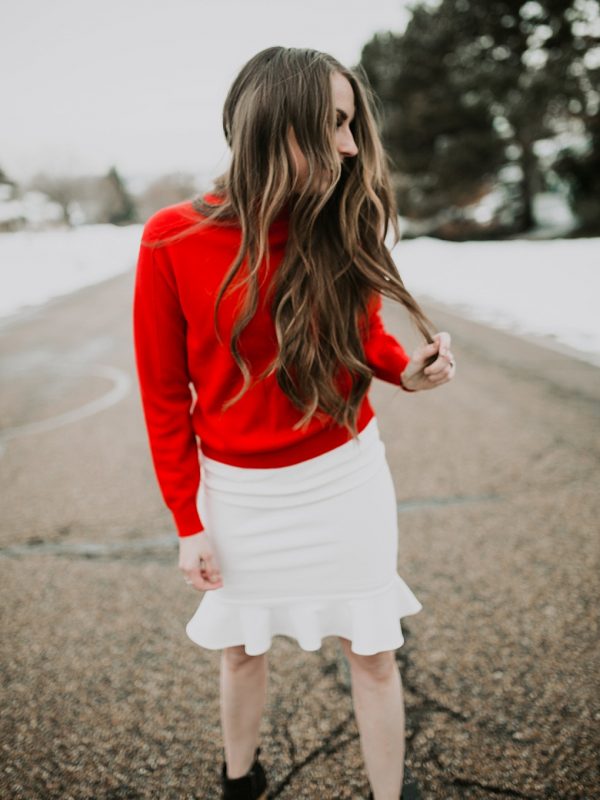red mockneck turtleneck with jeans and sneakers girl standing in snow with long loosely curled brown hair with caramel highlights