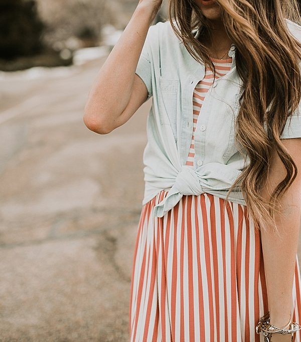girl standing in road in pink stripe dress downeast basics with denim button up shirt over top with long loosely curled brown hair