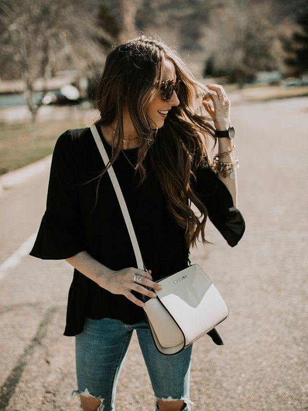 girl standing in road with karen walker sunglasses on with levi distressed high waisted jeans michael kors crossbody bag and flats on with loosely curled brown hair with caramel highlights